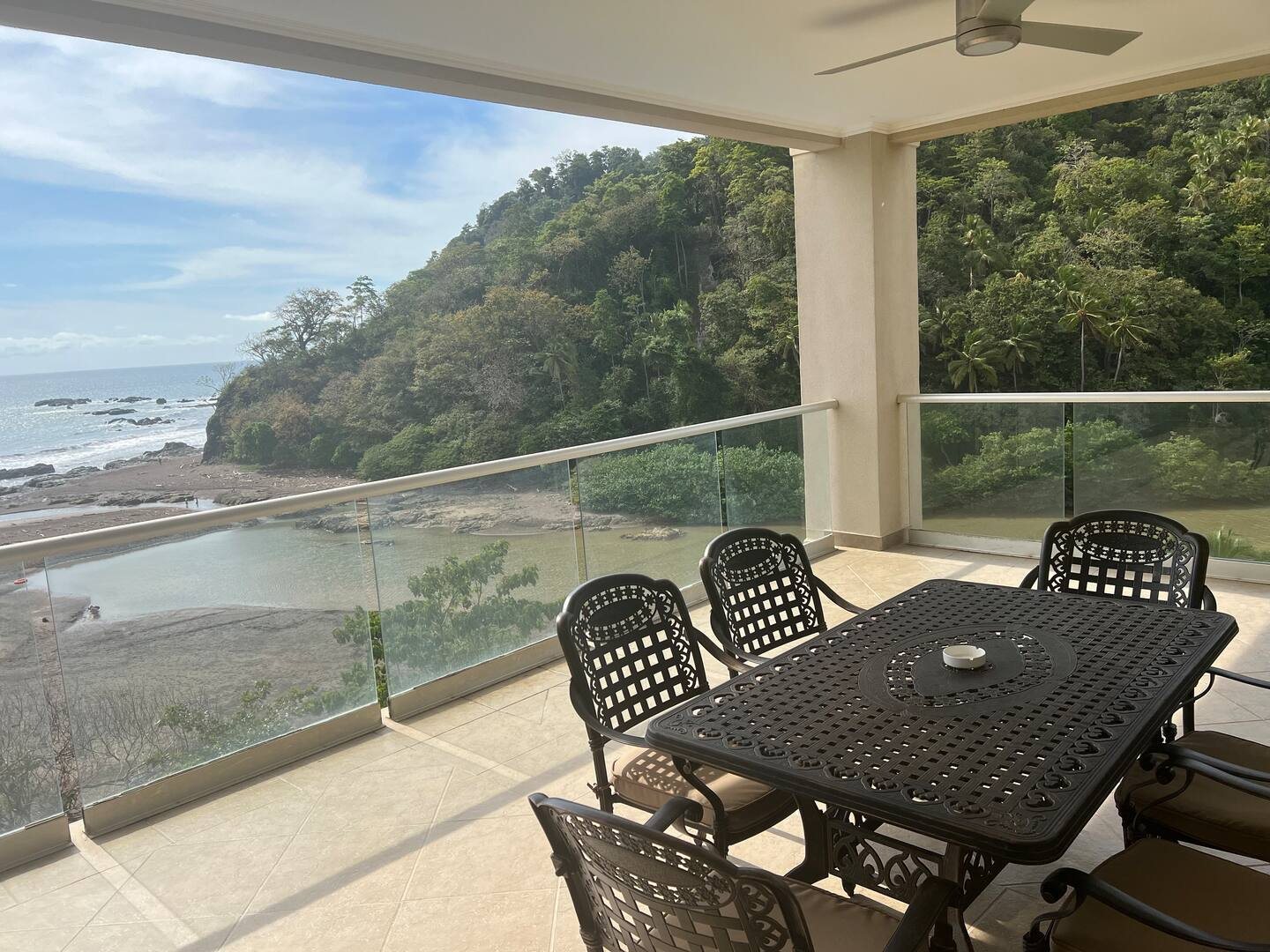 Covered balcony with a dining set overlooking the beach and forested tropical hills