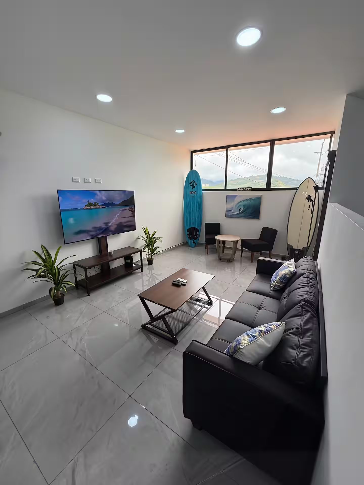 Modern living room with a sofa, television and decorative surfboards by large windows