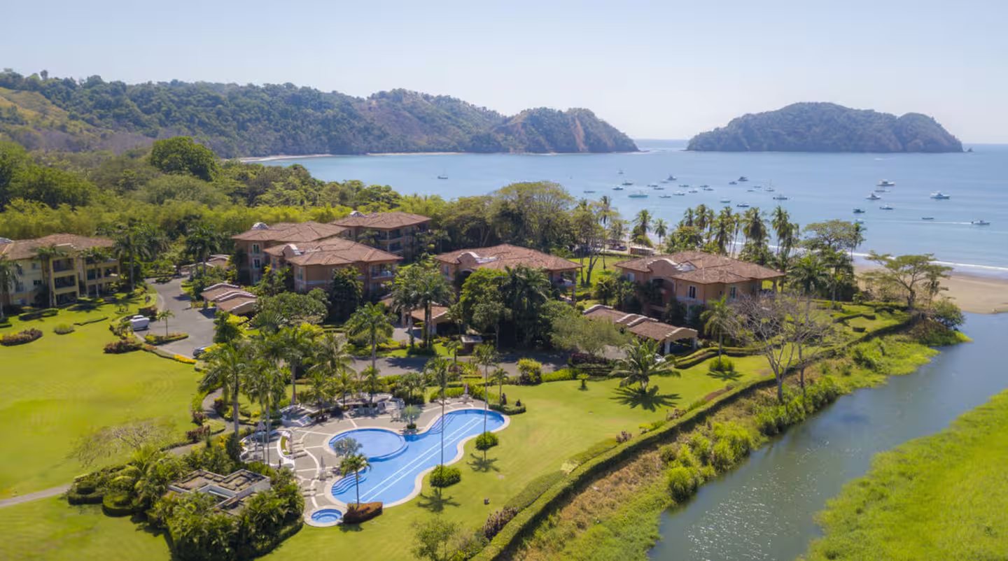 Coastal resort with red-tiled buildings and a pool above a boat-filled tropical bay
