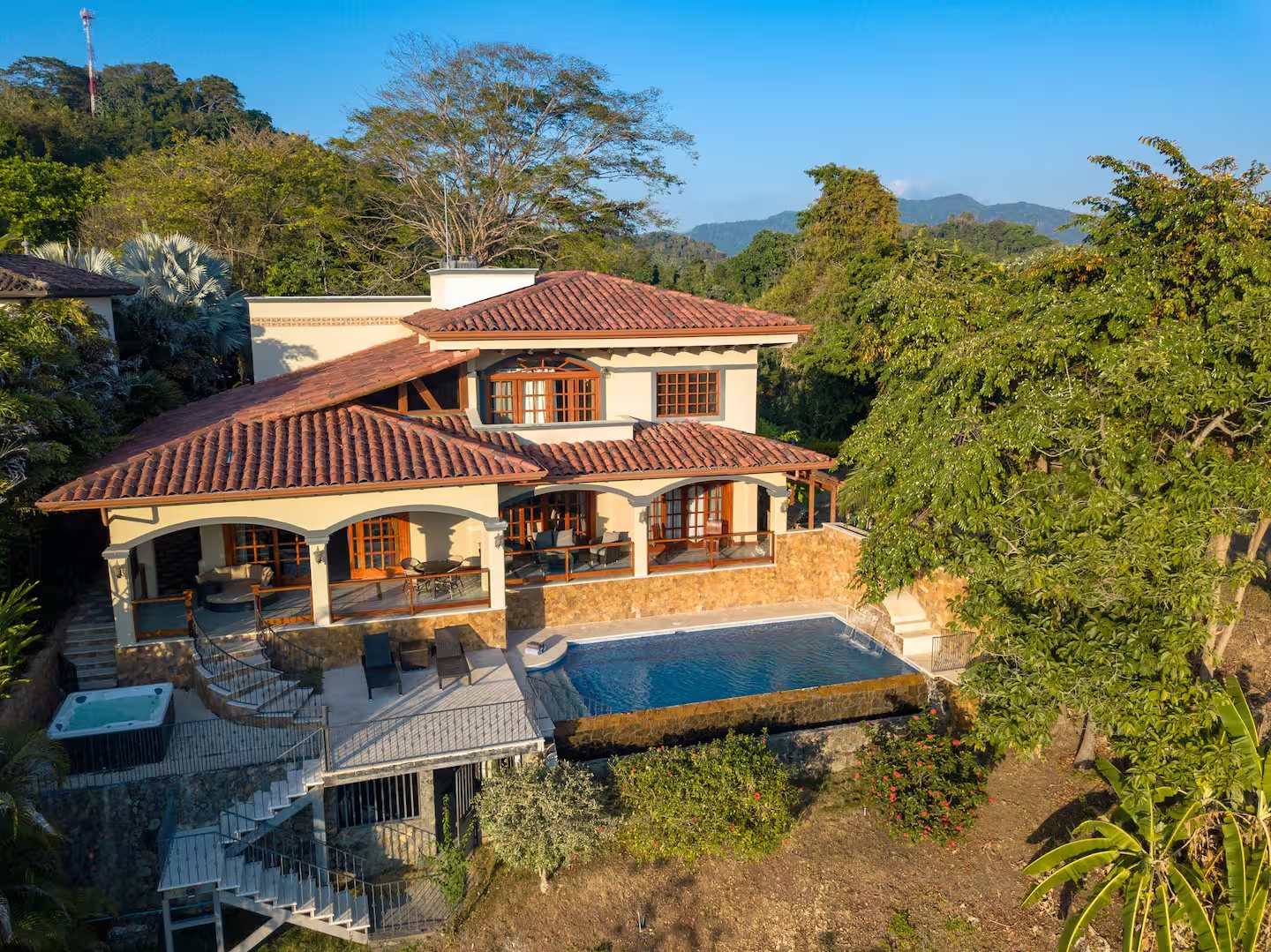 Mediterranean-style villa with red tile roofs, a pool and hot tub in tropical greenery